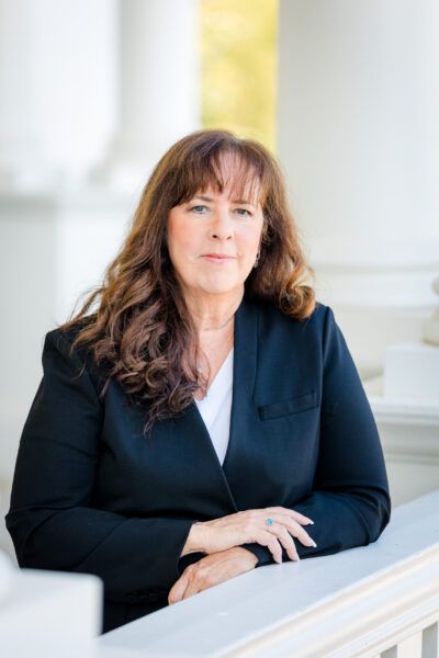 CEO Susan L. Wagner. White woman with long curly brown hair wearing a black blazer.