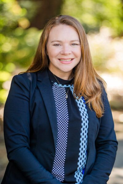 Angie Hendershot. White woman with red hair wearing a patterned blue blouse and navy blazer.