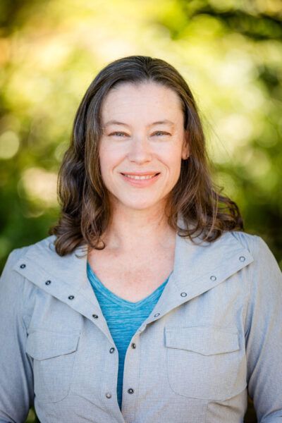 Tracy Cook. White woman with curly brown hair wearing a teal shirt and grey jacket.