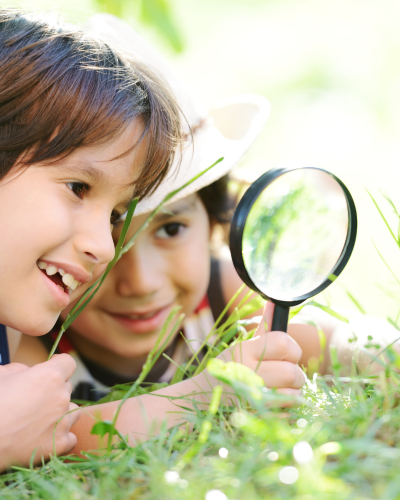 Two children look through magnifying glass at plants